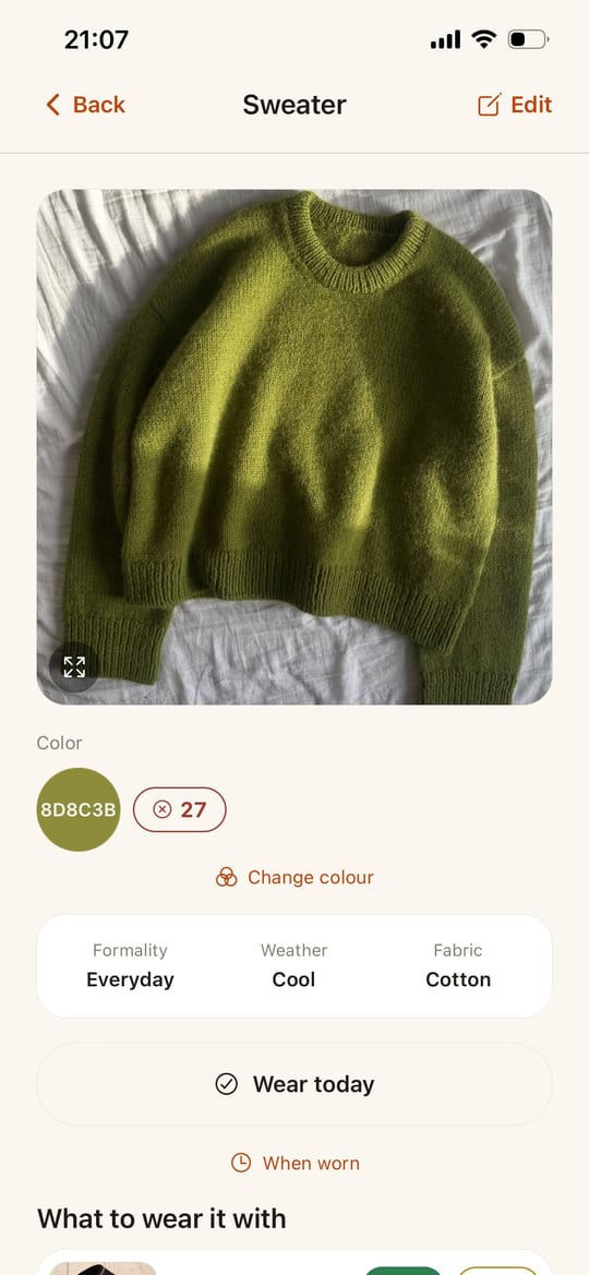 An item card in Ecru: a green jumper, its colour 8D8C3B, a “suits you” score of 27, and below that its formality, weather and fabric, with a “Wear today” button.